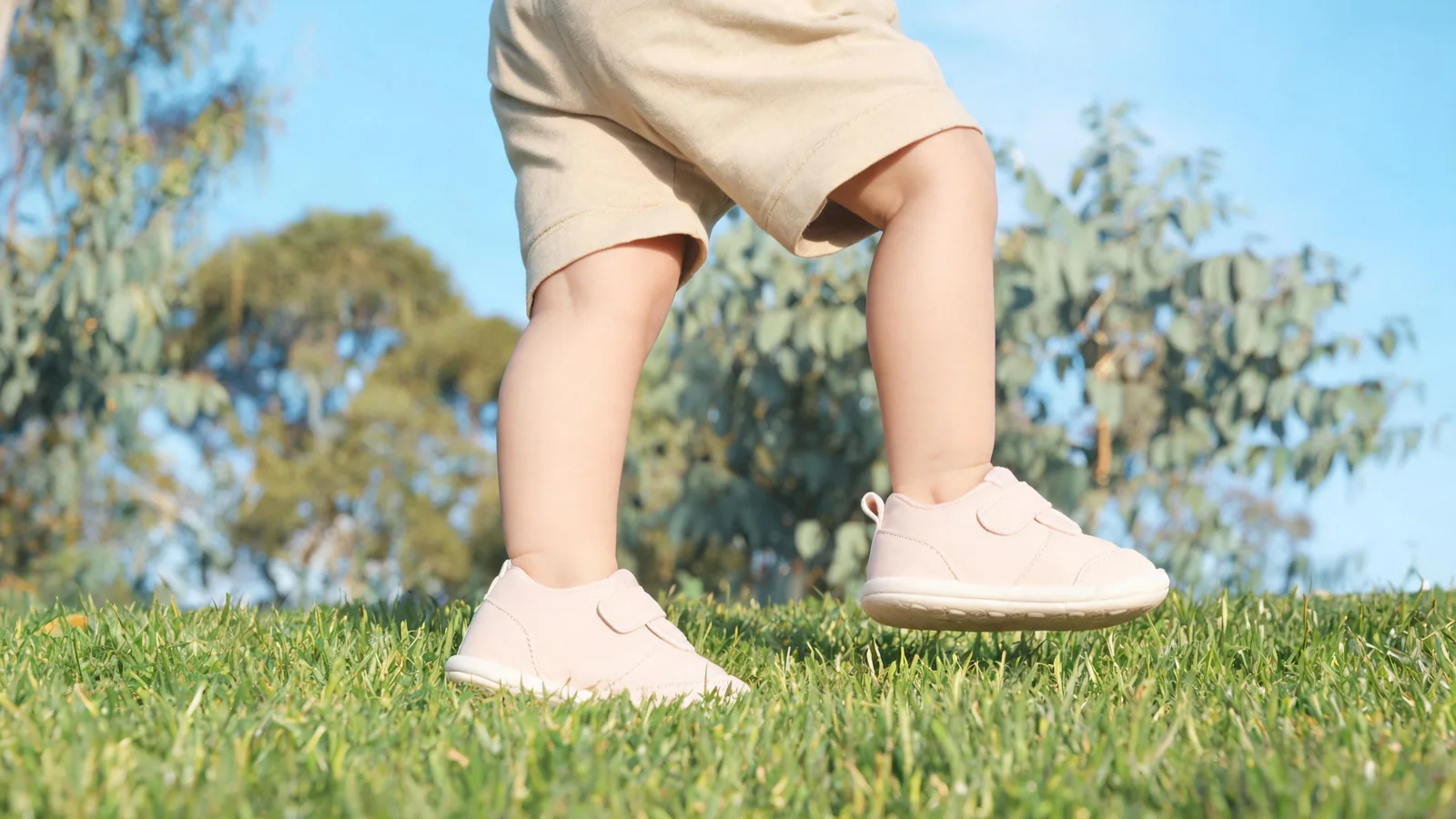 Toddler taking first steps outdoors in soft-sole first walker shoes